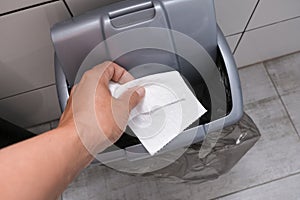 Human hand holding and throwing away a tissue, toilet paper to a bin in restroom