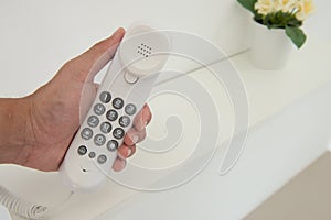 Human hand is holding the white office telephone