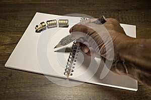 Human hand holding wooden pencil on blank notebook with golden train