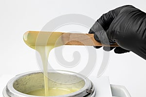 Human hand holding wooden sticks with wax over wax melter