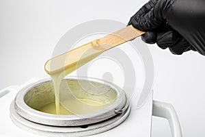 Human hand holding wooden sticks with wax over wax melter