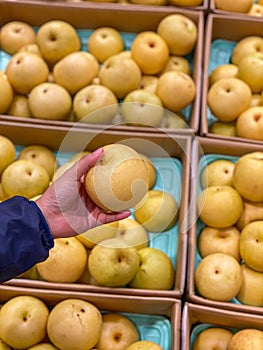 Human hand holding a yellow fresh pear at fruit store
