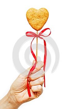 Human hand holds a homemade heart shaped cookie on a stick