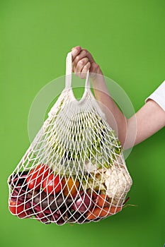 Human hand holds string bag mesh with vegetables and fruits. Zero waste shopping concept.