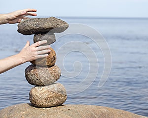 Human hand making stack of large round stones near the water