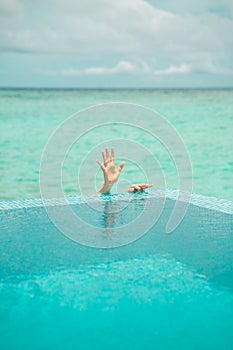 Human hand over water shot behind the edge of swimmig pool on background of Indian coean