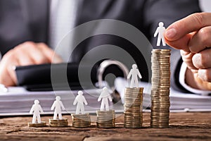 Human Hand Placing Human Figure On Increasing Stacked Coins