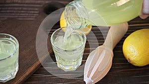 Human hand pouring Italian drink lemon liqueur limoncello in glass on the wooden table with bottle and lemon friuts