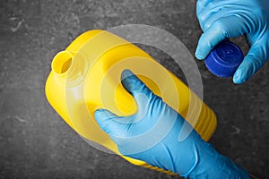 Human hand in protective glove holding a bleach bottle