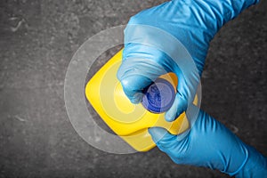 Human hand in protective glove opening a yellow bleach bottle