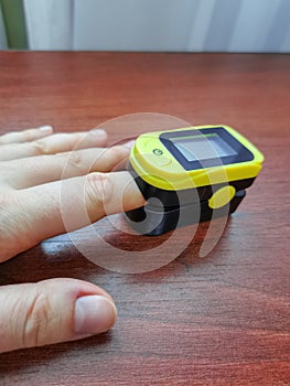 Human hand with a pulse oximeter on the index finger on a wooden background