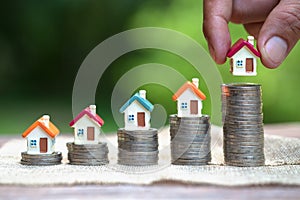 Human hand putting house model on coins stack. Concept for property ladder, home and residence, mortgage and real estate