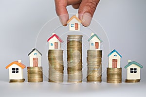 Human hand putting house model on coins stack. Concept for property ladder, mortgage and real estate investment