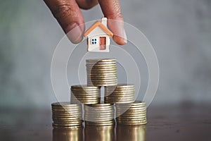 Human hand putting house model on coins stack, planning savings money of coins to buy a home concept, mortgage and real estate