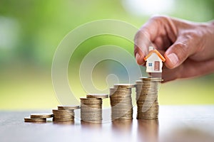 Human hand putting house model on coins stack,  planning savings money of coins to buy a home concept, mortgage and real estate