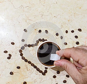 A human hand putting a sugar cube in a coffee cup