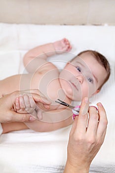 Human hand with scissors cutting baby nails on arms, scared infant lying on back