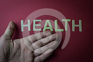 Human hand showing the word Health written with plastic letters on dark red paper background