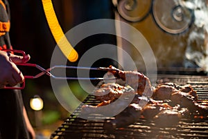a human hand turns chicken drumsticks on a barbecue grill with grilling tongs. cooking food on an open fire in the