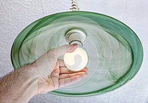 Human hand twists LED lamp into ceiling fixture green glass.