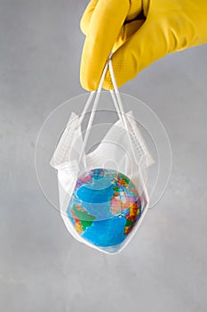 Human hand in yellow glove holds earth lying in medical mask on blue background