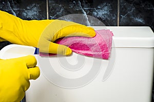 A human hand in a yellow rubber glove washes the cistern with a