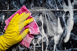 A human hand in a yellow rubber glove washes a tiled cloth