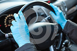 Human hands in blue medical gloves holding steering wheel. Protection against the Covid-19 virus