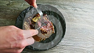 Human hands cut baked meat steak on halves by fork and knife