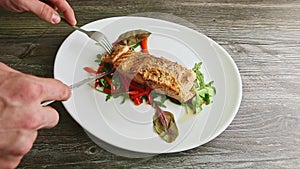 Human hands cut baked salmon fillet with fork and knife
