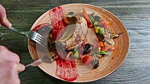 Human hands cut off small piece from barbecued meat rib by knife on plate