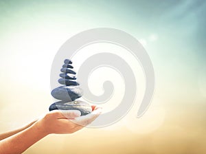 Human hands holding balanced rocks over sunset beach