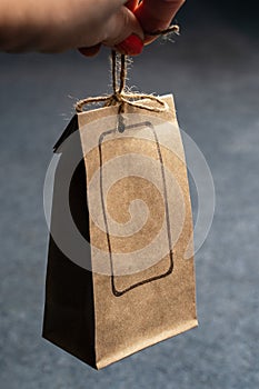 Human hands holding craft cardboard pack packages tied with raw twine, with empty frame for logo stamped on side, on dark grey bac