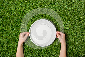 Human hands holding empty paper plate on grass