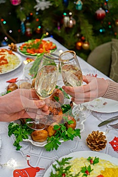 Human hands holding glasses with sparkling wine. Friends or family toasting with champagne against festive Christmas table and