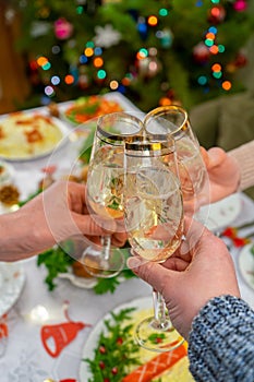 Human hands holding glasses with sparkling wine. Friends or family toasting with champagne against festive Christmas table and