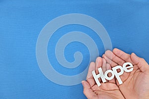 Human hands holding hope word cutout in blue background. Top view with copy space.