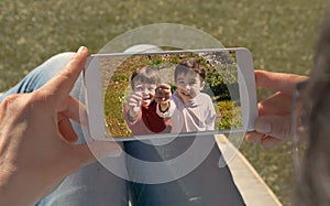 Human hands holding mobile looking at a picture of two twin children