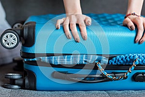 human hands holding overloaded suitcase with wheels on sofa