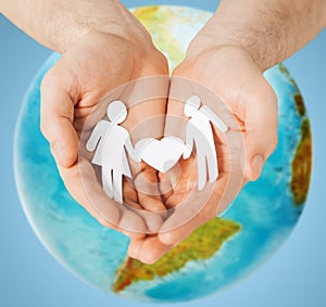 Human hands holding paper couple over earth globe