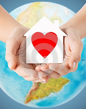 Human hands holding paper house with red heart