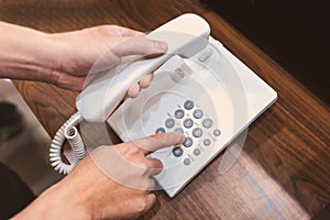 Human hands holding telephone handle and dialing on wooden table