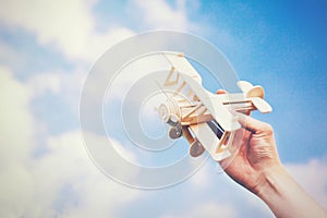 Human hands holding a wooden plane toy over blue sky with copyspace