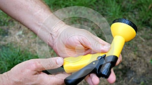 Human hands insert a yellow garden sprayer into new green rubber hose.