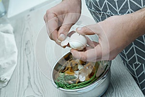 Human hands peeling shell of boiled egg over bowl of vegetable peelings. Protein product. Separate waste collection.
