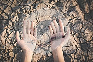 Human hands praying for the rain on cracked dry ground