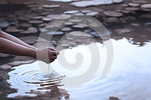 Human hands scoop water from a parched pond, underscoring the global water crisis caused by climate change and the shortage of