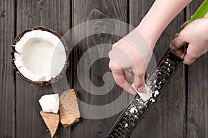 Human hands slashing coconut pieces with grater on wooden background