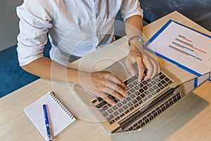 Human hands typing laptop keyboard next to graph document