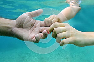 Human hands in underwater. Baby hand holding fathers finger. Underwater hands of father and small child in clear blue